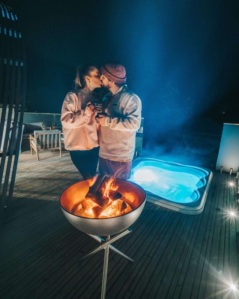 A couple enjoy a kiss by the fire pit at SeaBeds Luxury Lookouts at Woodlands Glencoe.