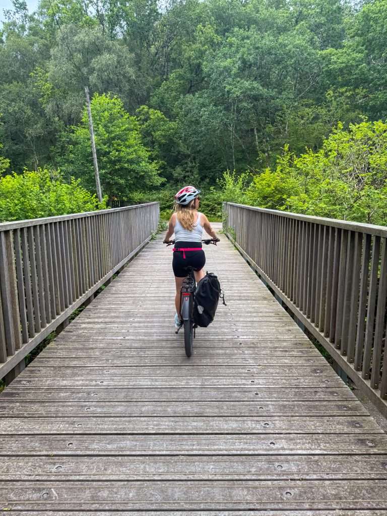 The Caledonia Way offers off-road cycle tracks through beautiful countryside. A lady rides an e-bike over a bridge.