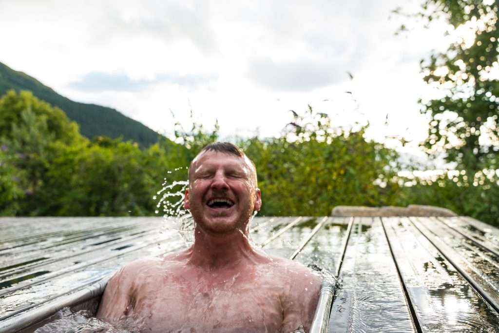 A man is smiling sitting in a plunge pool at the Woodlands Wilderness Sauna.