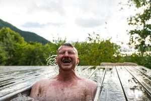 A man is smiling sitting in a plunge pool at the Woodlands Wilderness Sauna.