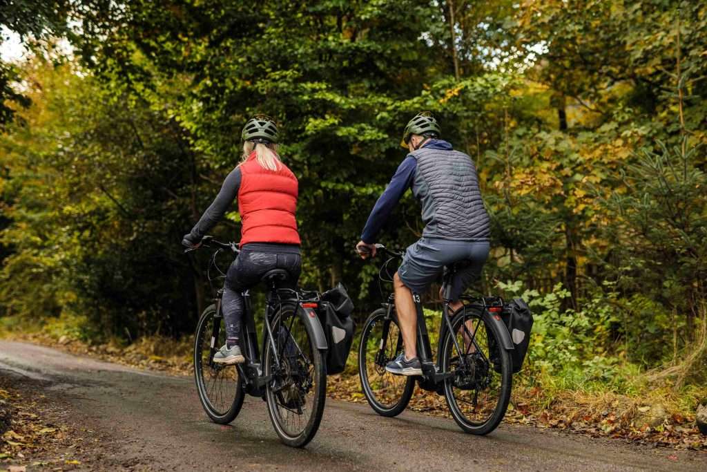 Couple on electric bikes cycling away from E-Bike hire at Woodlands Glencoe, Scotland.