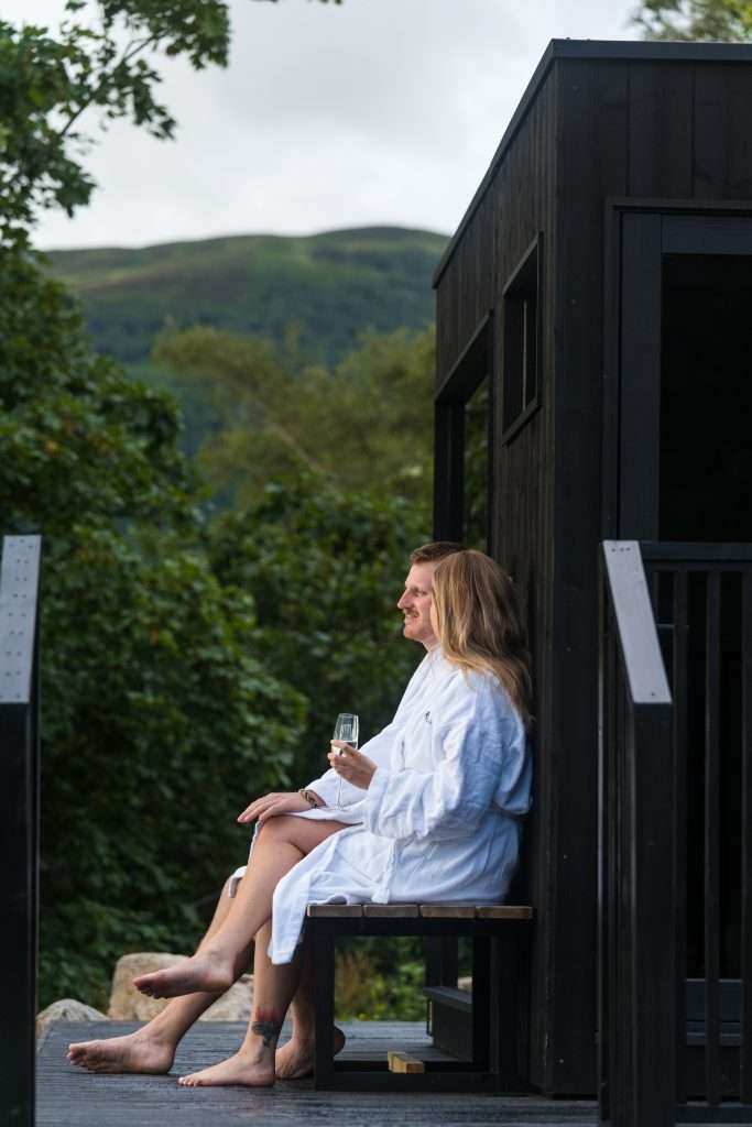 A couple enjoy the view outside the Wilderness Sauna at Woodlands Glencoe.