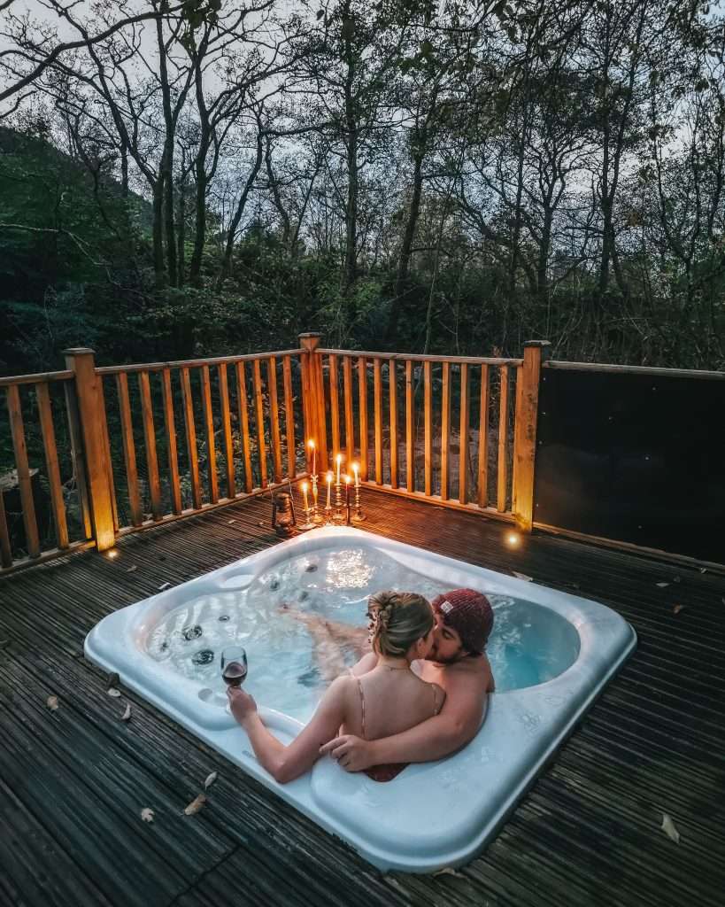 A couple enjoy a drink by candle light in a hot tub at RiverBeds Luxury Wee Lodges at Woodlands Glencoe.
