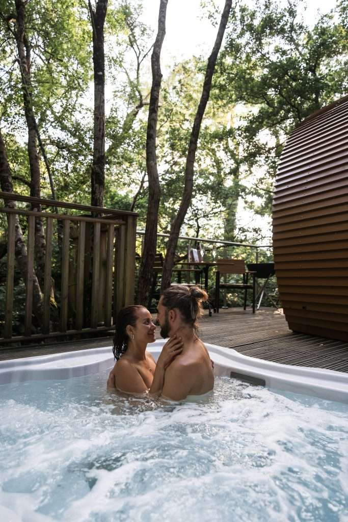 Romantic RiverBeds Luxury Wee Lodges at Woodlands Glencoe. A couple share a cuddle in the hot tub on the terrace of the cabin.
