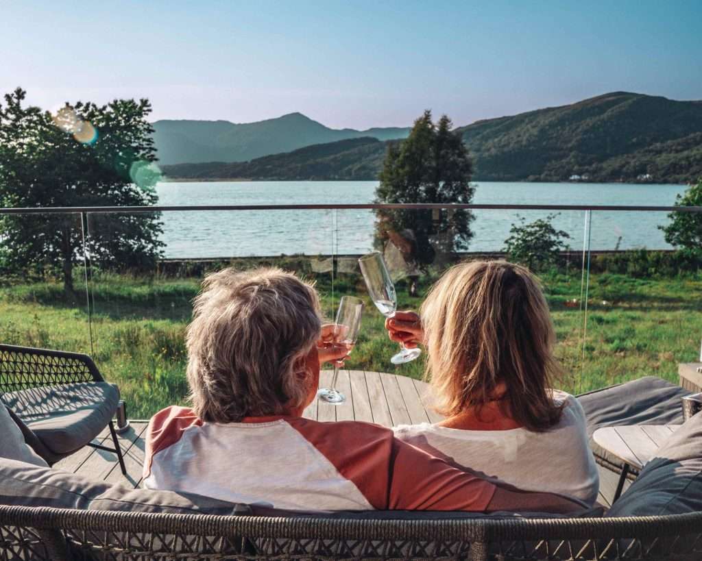 Couple toasting at Romantic Luxury Lodge with Hot Tub in Glencoe, Scotland. Fantastic mountain and loch view in background.