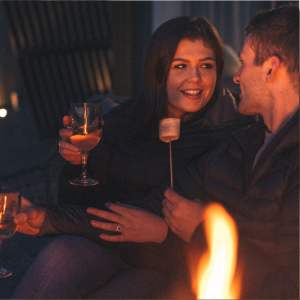 A couple toast marshmallows outside SeaBeds Luxury Lookouts at Woodlands Glencoe.