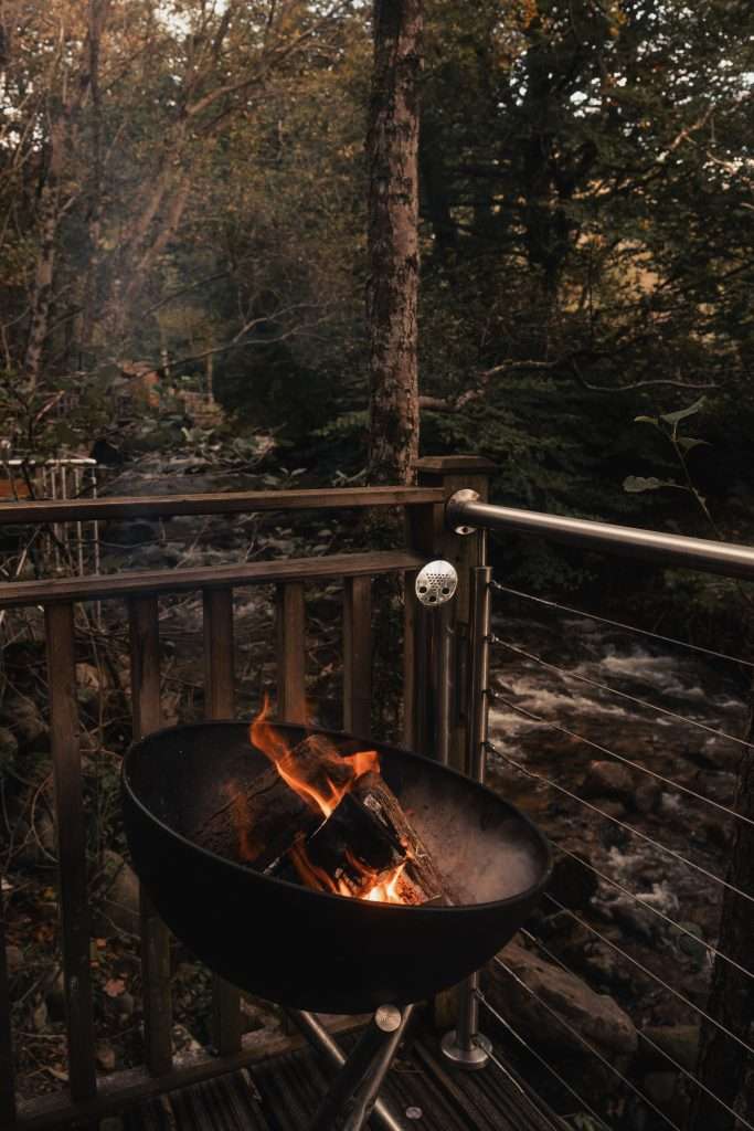 A fire pit crackles on the terrace of RiverBeds Luxury Wee Lodges at Woodlands Glencoe.