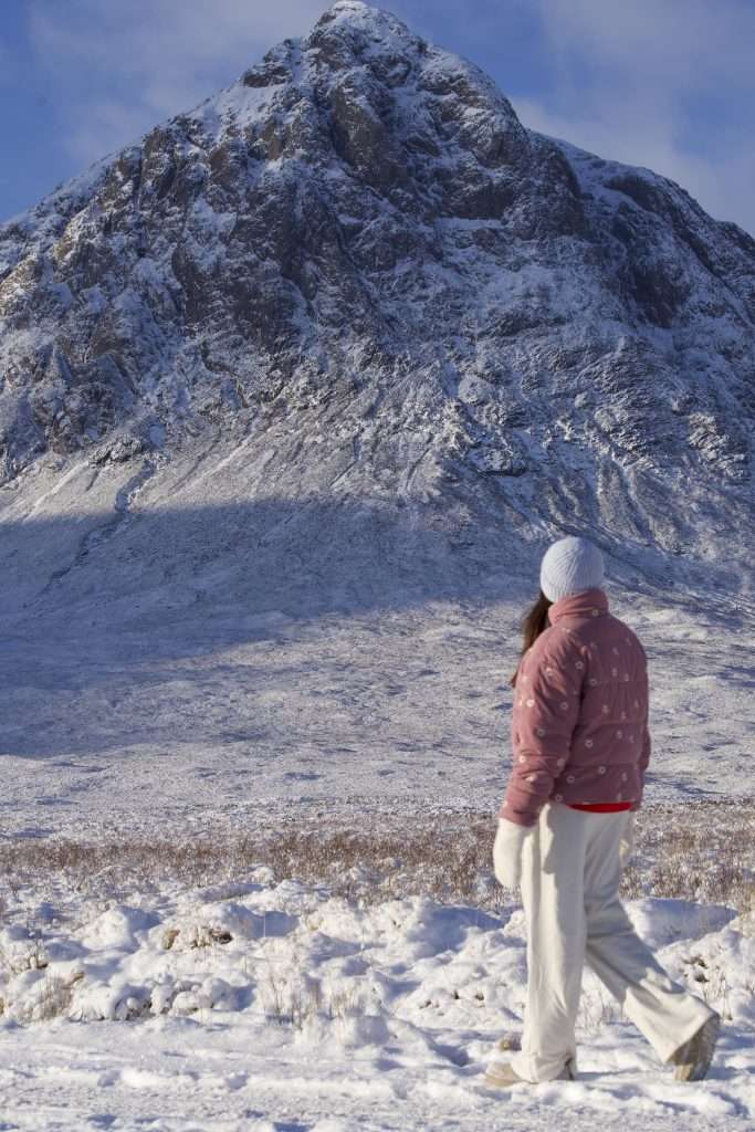 A woman goes for a snowy walk beneath Buachaille Etive Mor in Glencoe.