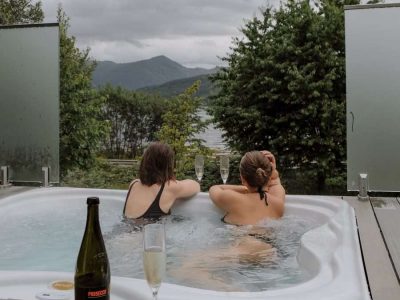 hottub-lodge-luxury-woodlands-glencoe A couple enjoy the loch and mountain view from the infinity hot tub at SeaBeds Luxury Lookout Lodges at Woodlands Glencoe. Extra romantic with prosecco and strawberries.