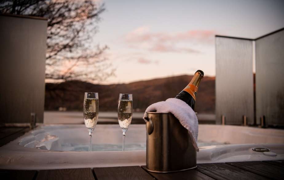 Champagne for two by the infinity hot tub with mountain and loch view at the romantic SeaBeds Luxury Lookout Lodge at Woodlands Glencoe.