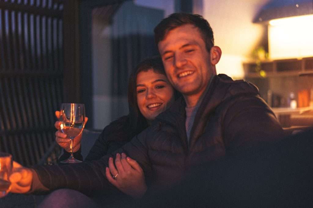 A happy couple enjoy a romantic evening under the stars with wine and fire pit at SeaBeds Luxury Lookout Lodge with Hot Tub at Woodlands Glencoe.