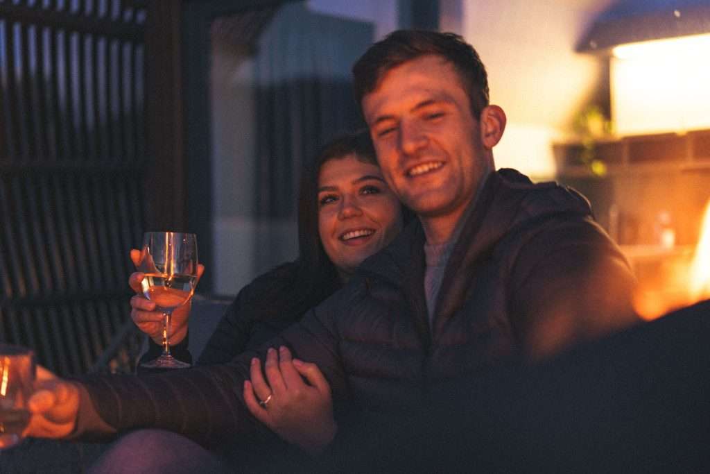 A happy couple enjoy a romantic evening under the stars with wine and fire pit at SeaBeds Luxury Lookout Lodge with Hot Tub at Woodlands Glencoe.