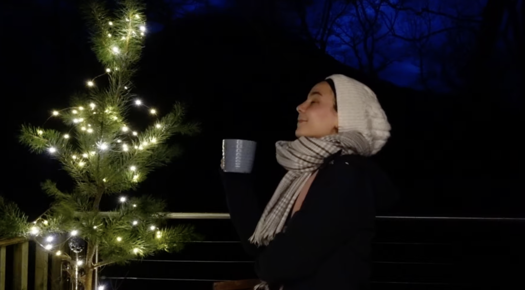 A lady enjoys a cup of coffee at RiverBeds Luxury Wee Lodges in Glencoe by the Christmas tree.